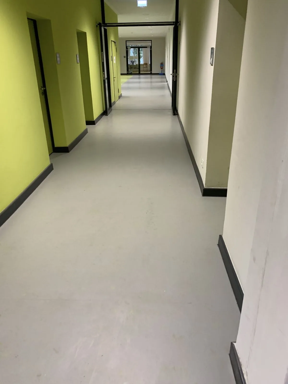 Neuer grau-grüner Bodenbelag mit schwarzem Sockel im Flur eines Berliner Schulgebäudes nach der Sanierung durch MANOVA